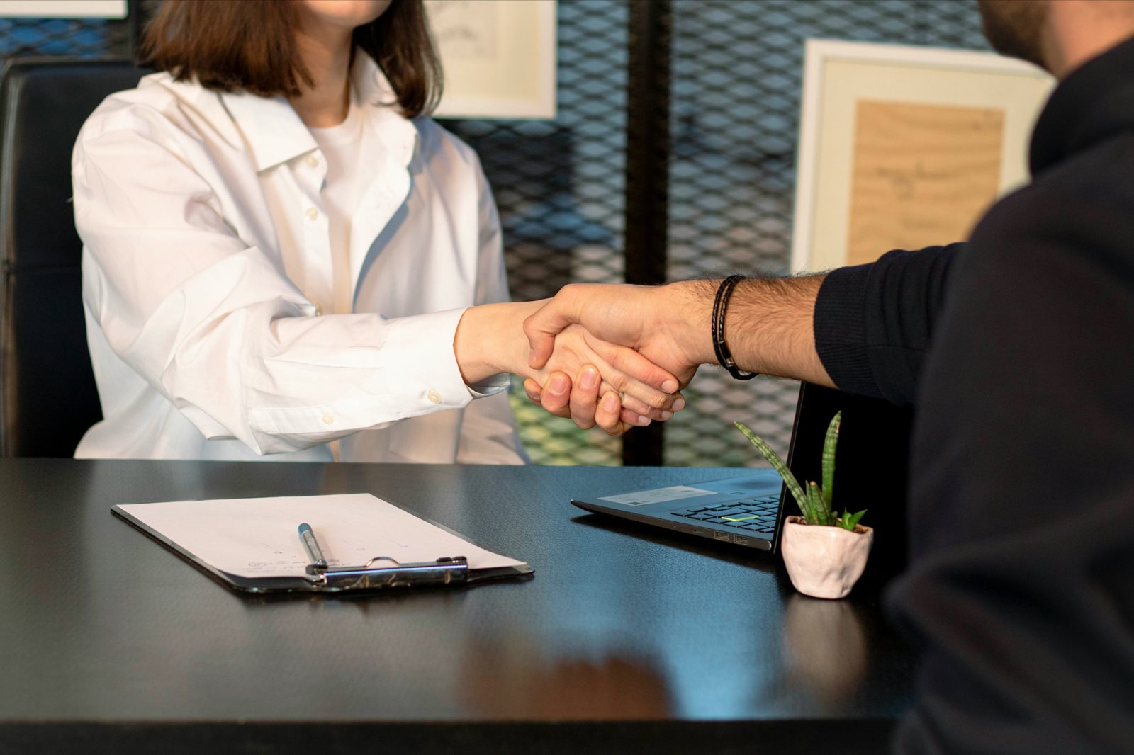 An adjustment of status lawyer and his client shaking hands across a desk, the filing paperwork between them