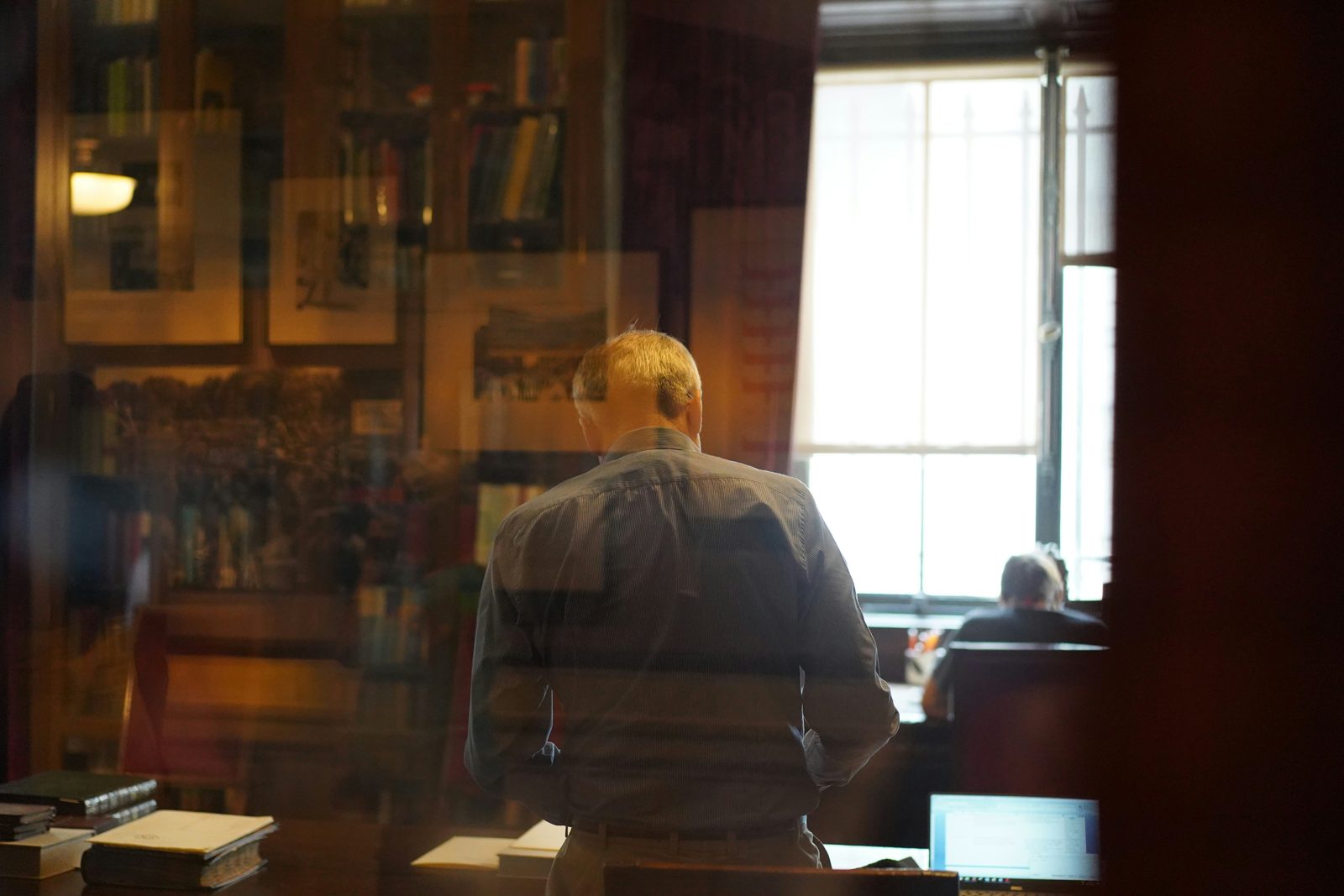 A DACA lawyer working at his desk, seen through the window of a book-lined office