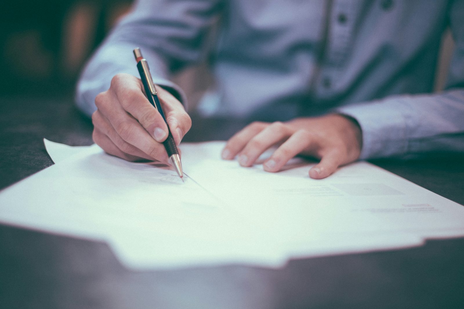 Hands going through an immigration application page by page, pencil in hand, during a document review