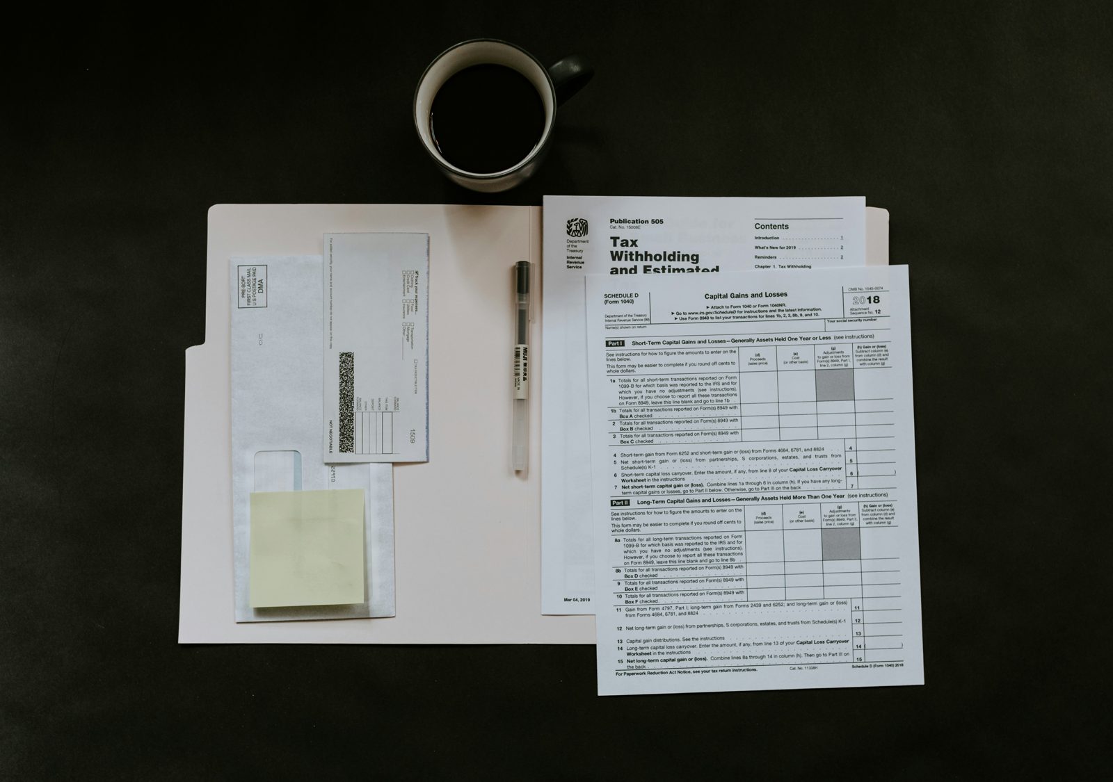 Employment paperwork on an employer's desk beside a coffee: a tax withholding form, an envelope and a pen