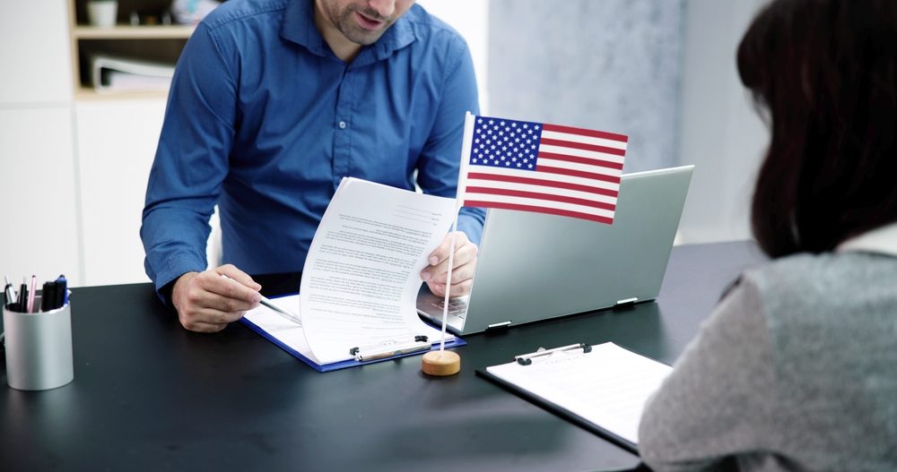 A green card lawyer going through an application with a client across a desk, a small US flag beside them
