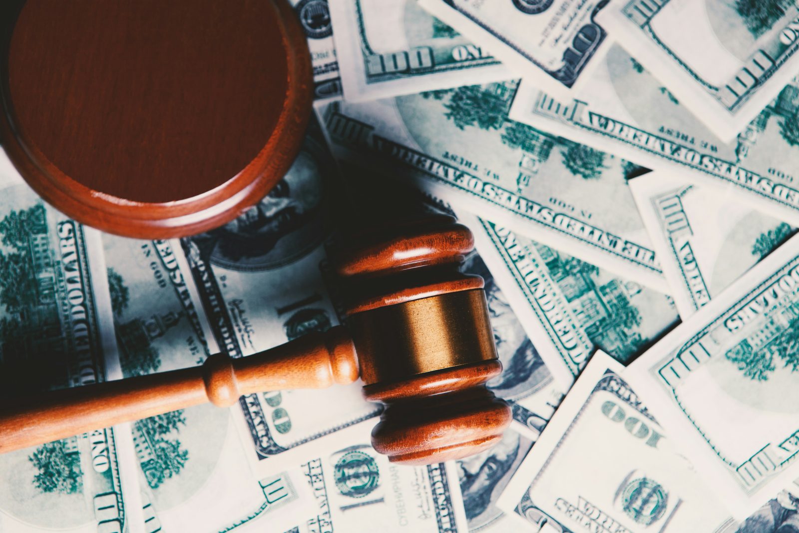 A gavel resting on a spread of hundred dollar bills, standing for the fines an I-9 audit can carry