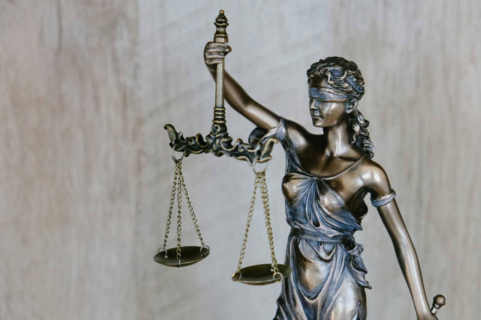 A bronze statue of blindfolded Justice holding up her scales against a pale stone wall