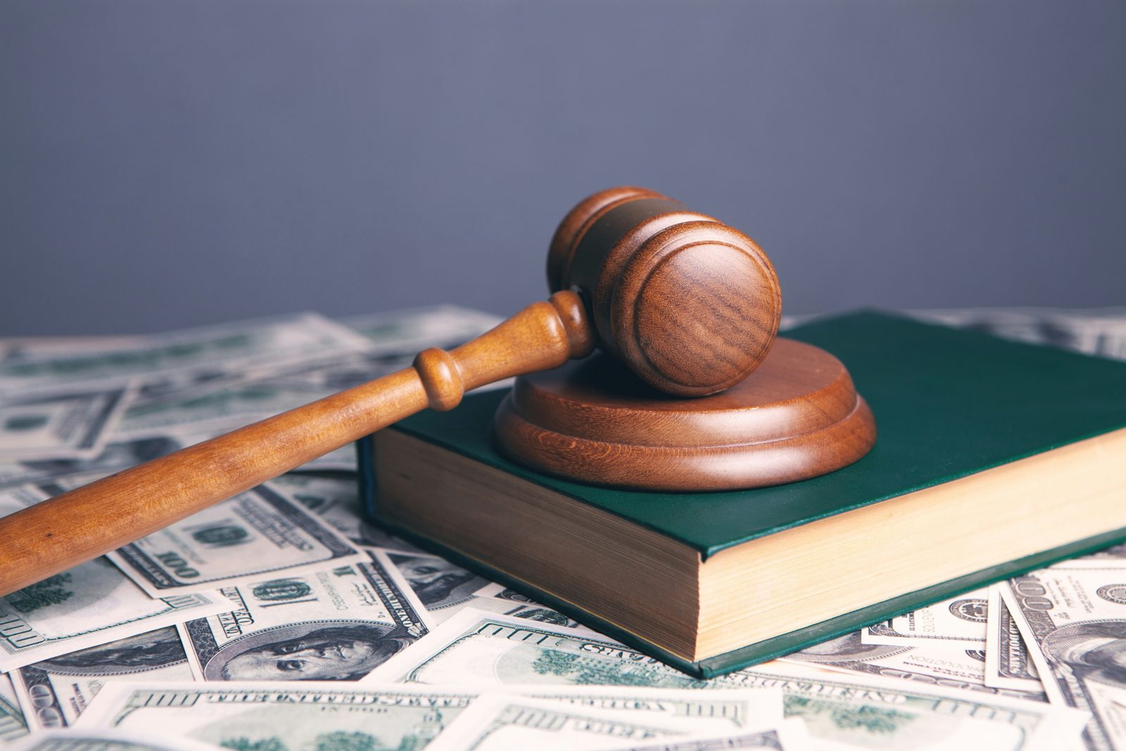 A gavel and a bound law book resting on a spread of hundred dollar bills