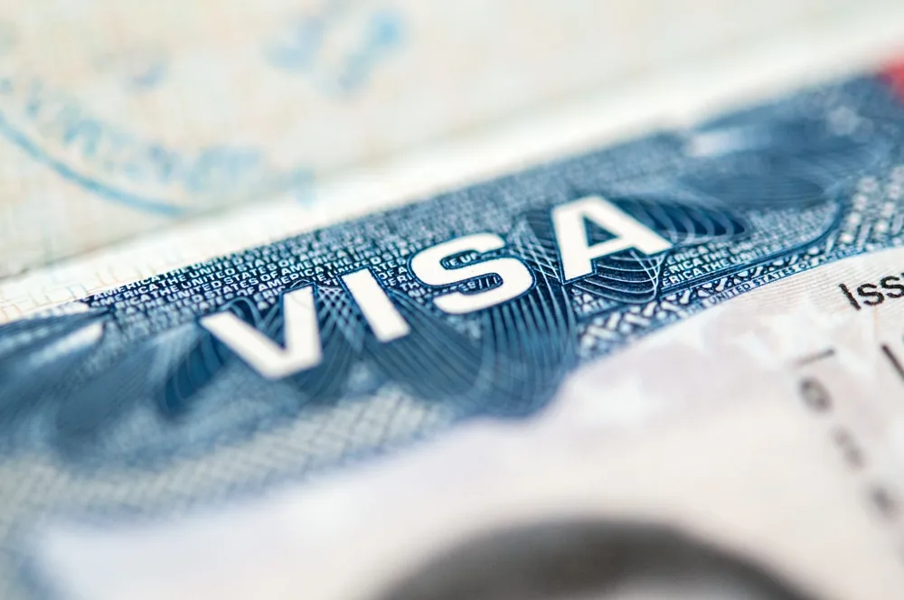 Close-up of a United States visa in a passport, the word VISA in blue security print beside a faded entry stamp